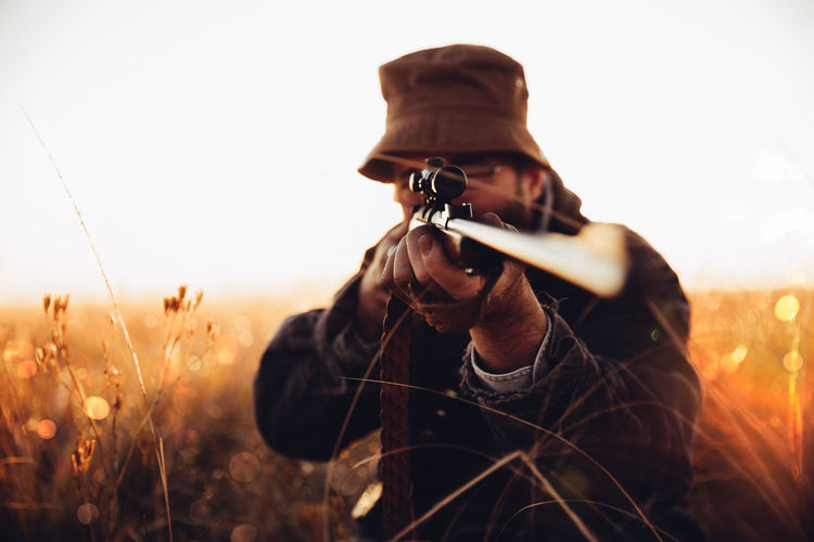 Man aiming rifle on field against sky