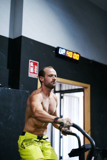 Fit shirtless young man working out in a bike at indoors gym