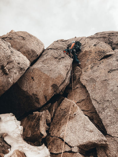 Climber ascending steep rock face with crampons secured by rope