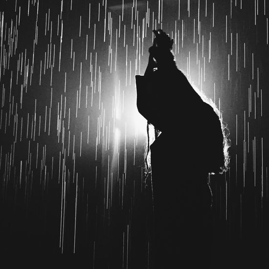 Side view of silhouette woman standing against sky at night during rainfall