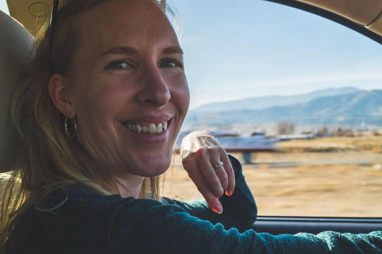 Smiling woman looks at camera while driving on road trip, view of desert out of drivers window