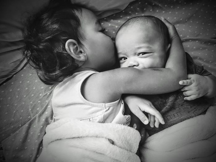 Cute girl with baby embracing on bed at home