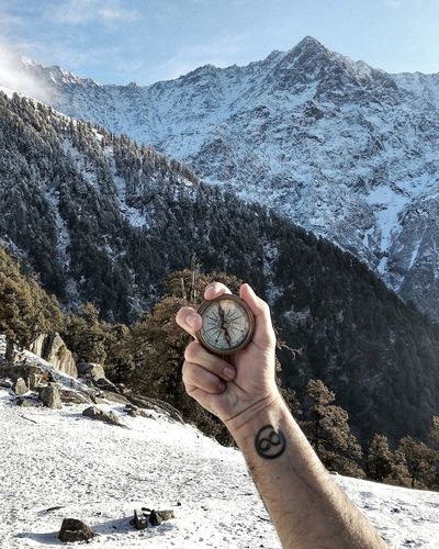 Cropped hand holding navigational compass on snowcapped mountain