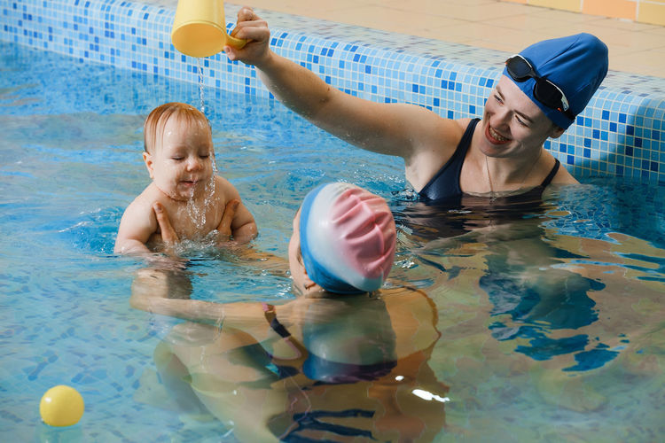 Early swimming coach training to swim baby boy in indoor pool playing activity for infant  mother