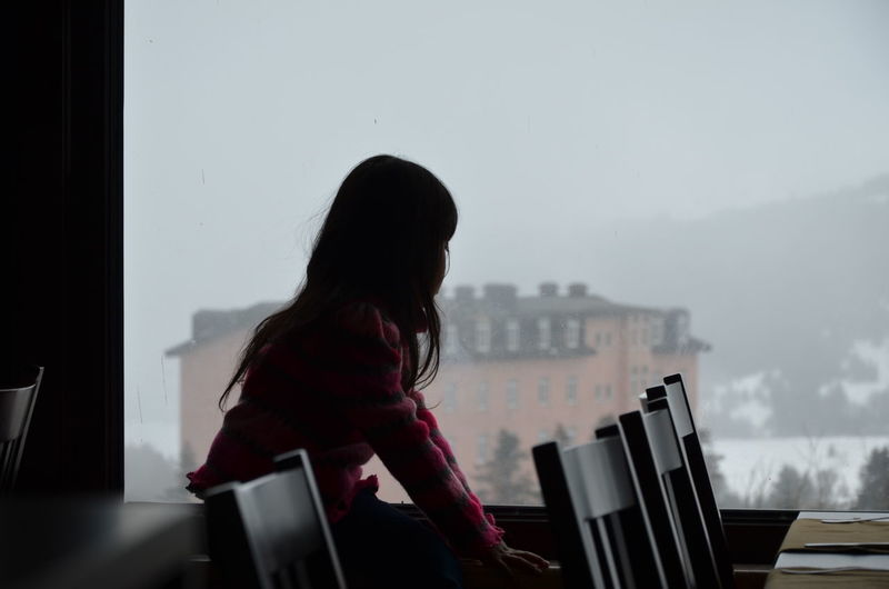 Little girl  standing by window against sky