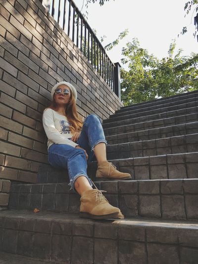 Portrait of young woman sitting on staircase against brick wall