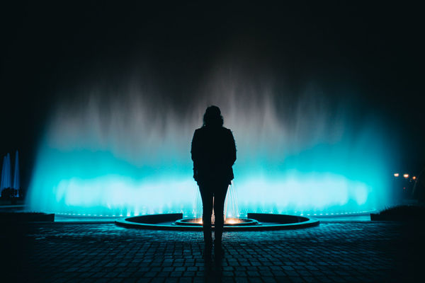 Rear view of silhouette woman standing by illuminated fountain at night