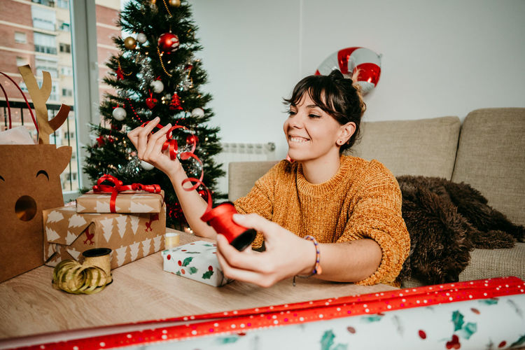 Young woman sitting by christmas tree at home