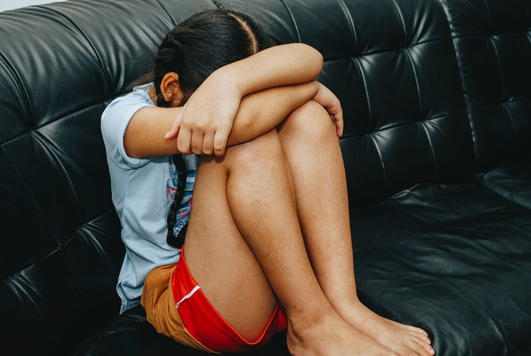 Girl with head on knees sitting on sofa at home
