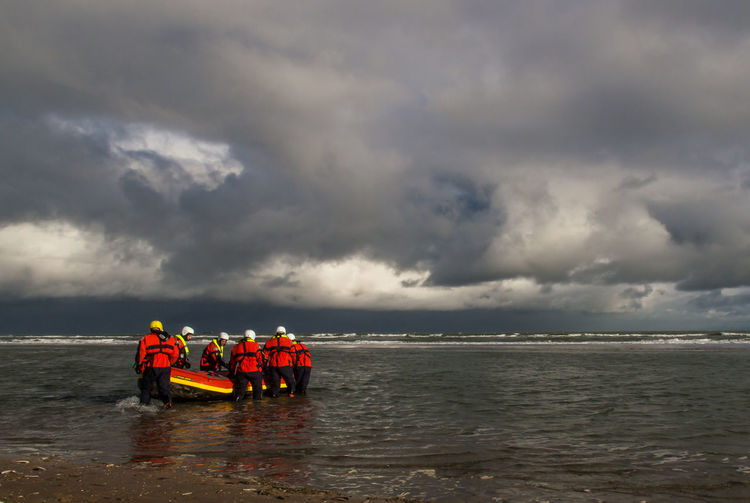 People wearing life jackets rafting in sea against cloudy sky