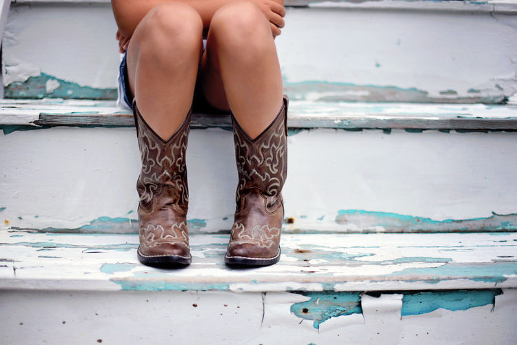 Low section of girl wearing cowboy boot while sitting on wooden steps