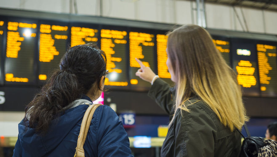 Rear view of female friends looking at arrival departure board
