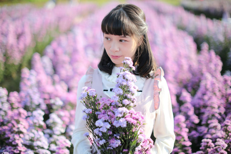 Beautiful woman looking away while standing by purple flowering plants
