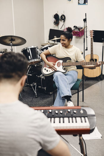 Smiling woman practicing guitar while rehearsing with man in classroom