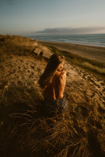 Rear view of woman crouching on field against sea