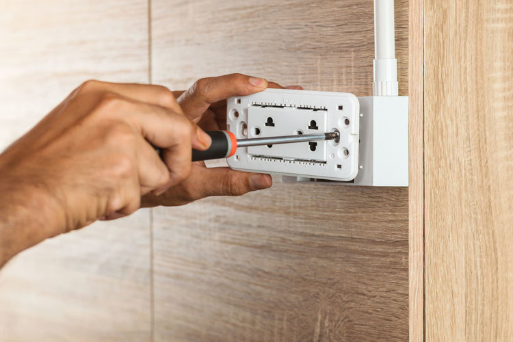 Using a screwdriver to install the electric power socket in to a plastic outlet box on a wooden wall