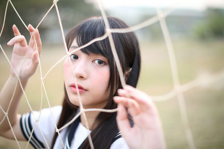 Portrait of young woman standing by sports net
