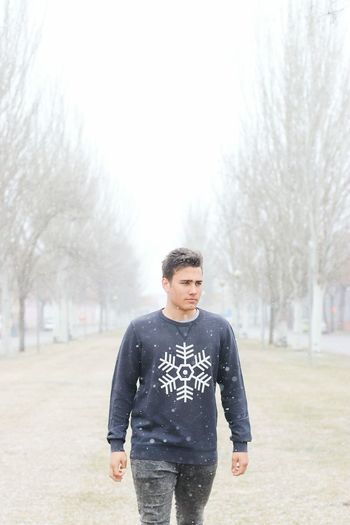 Young man walking on field at park during snow fall