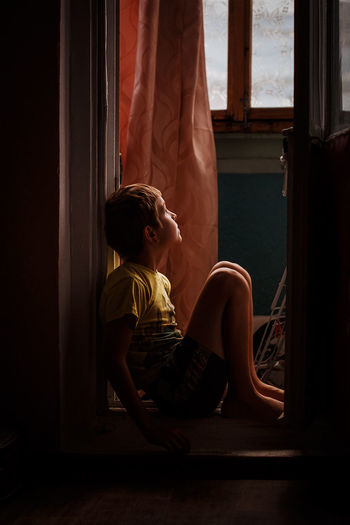 Side view of boy sitting at doorway at home