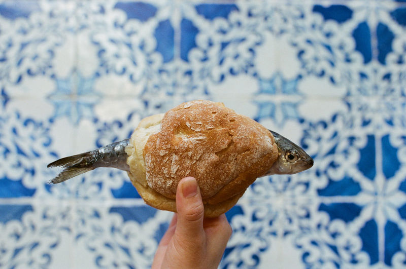 Cropped hand holding bread with fish against wall