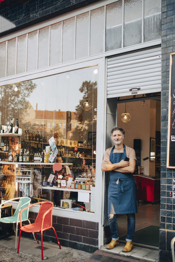 Full length portrait of male owner standing at entrance of deli