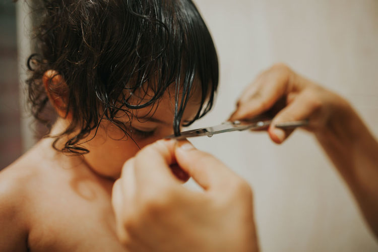 Cropped hands of mother cutting girl hair at home