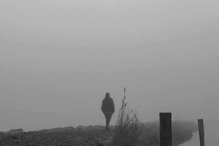 Rear view of man walking on landscape against clear sky