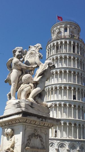 Statues and leaning tower of pisa against clear blue sky