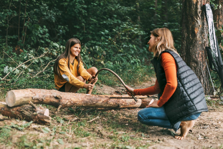 A mother and her daughter are sawing a fallen tree for a fire. firewood harvesting, bonfire, picnic