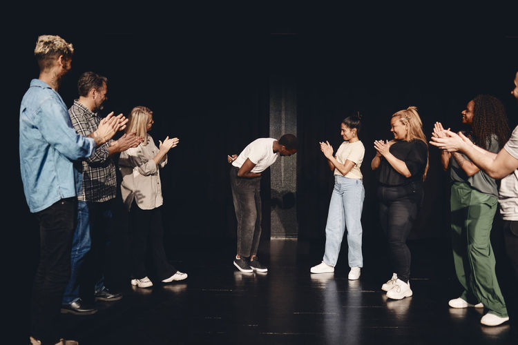 Multiracial male and female artists applauding for actor bowing on stage