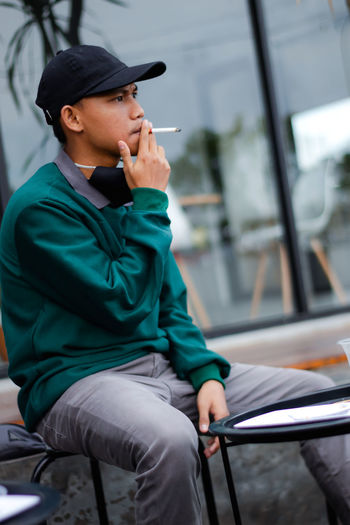 A grown man is sitting and smoking a cigarette