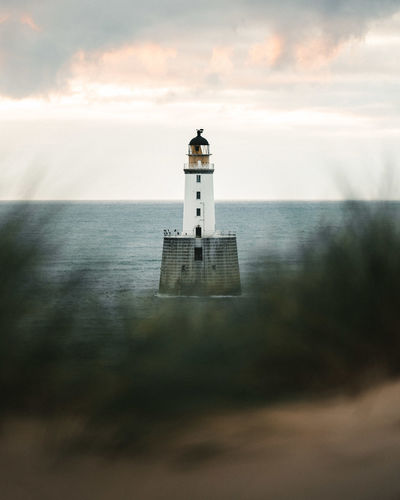 Lighthouse on building by sea against sky