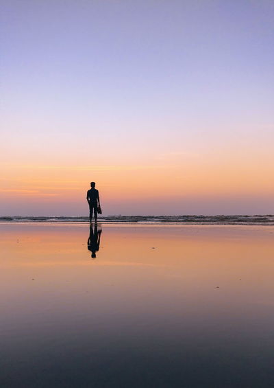 Silhouette man standing on shore at beach against sky during sunset