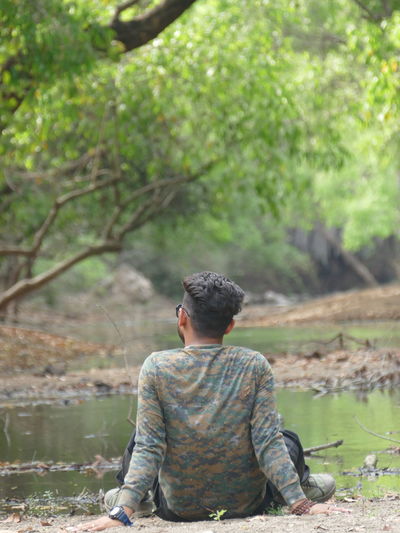 Rear view of man sitting on rock