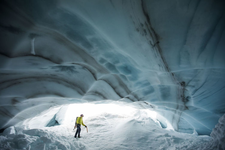 Ice climber looks up at the ceiling of a glacial ice cave in canada.