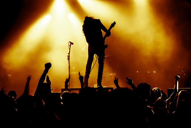Silhouette crowd enjoying while guitarist playing guitar on stage during concert