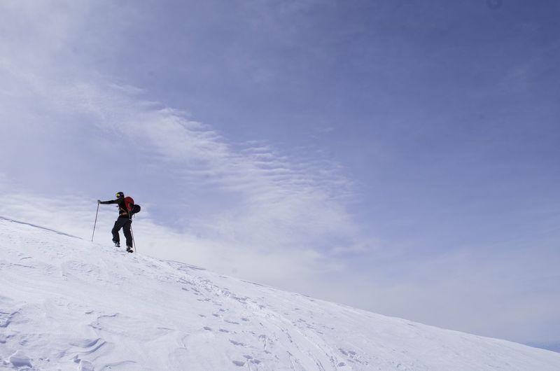 Full length of skier on snowcapped mountain against blue sky - mountain climbing