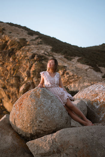 Woman leaning on rock against sky