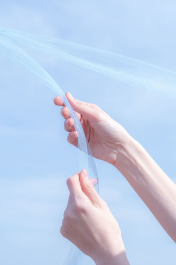 Cropped hand of woman holding hands against blue sky