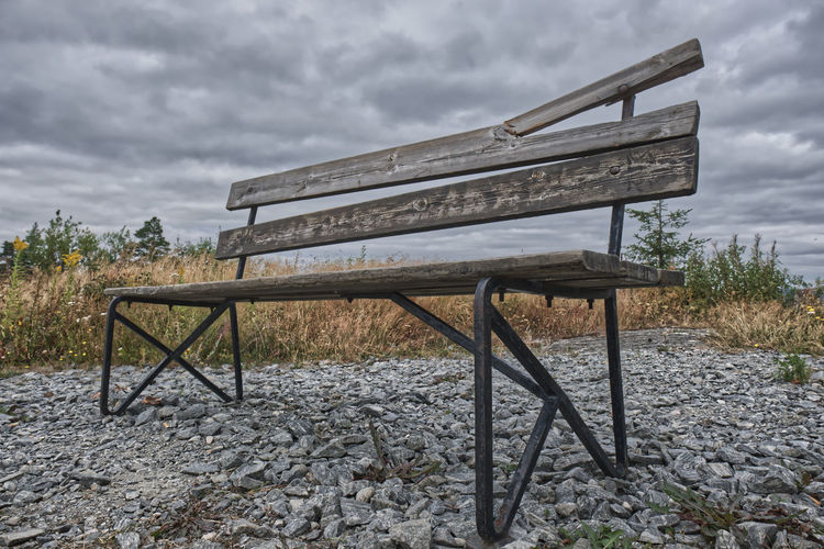 Empty bench on field against sky