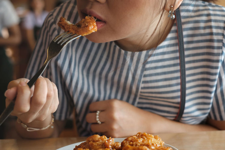 Midsection of young woman eating food in restaurant