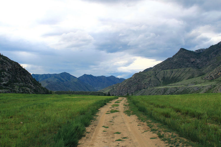 The road in a wide alpine gorge in altai against the background of high mountain ranges in summer