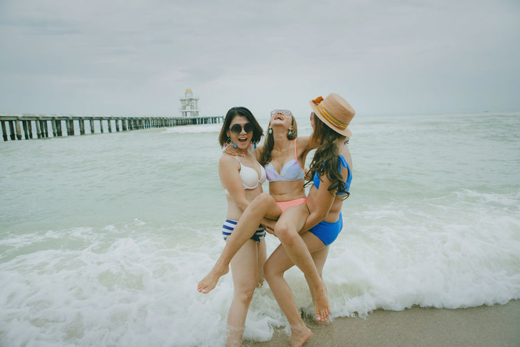 Women lifting friend at beach against sky