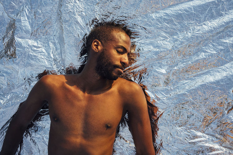 Shirtless man sleeping while lying on silver aluminum foil