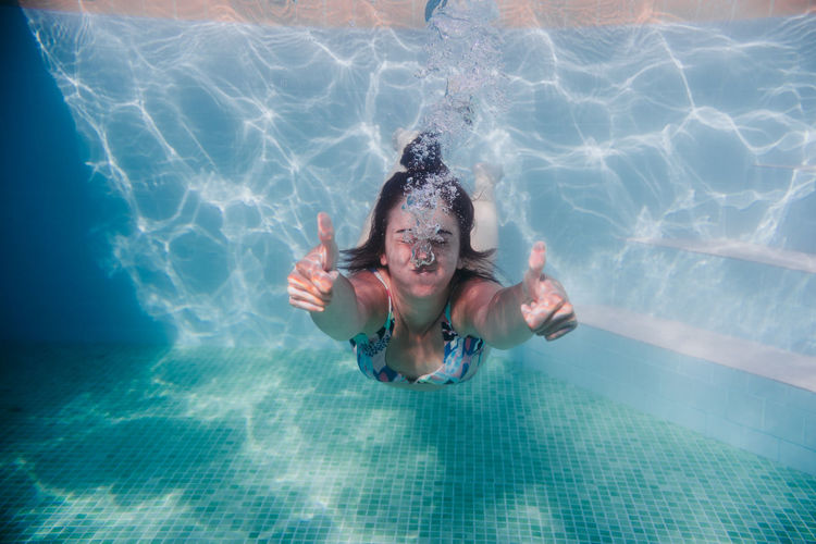 Woman gesturing while swimming underwater in pool