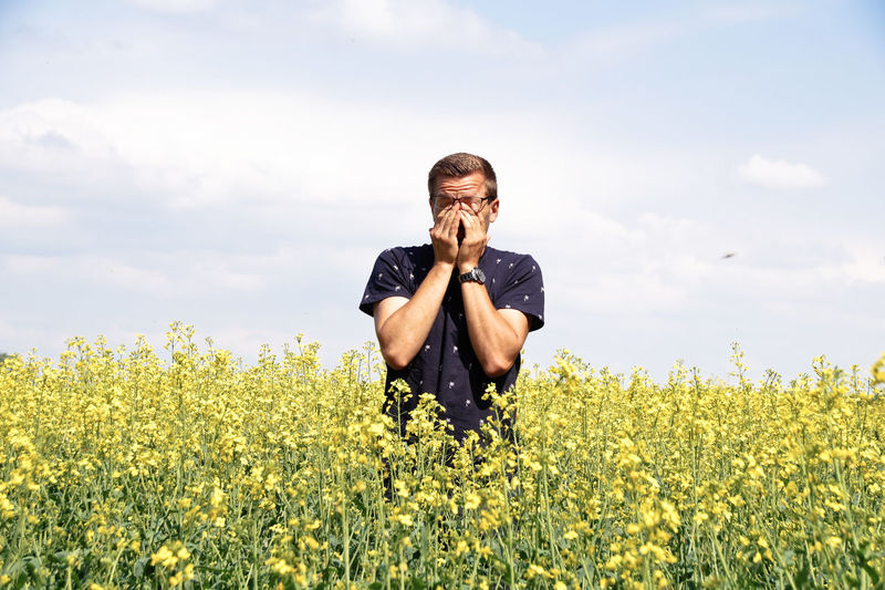 Man cleaning eyes while standing amidst flowering plants