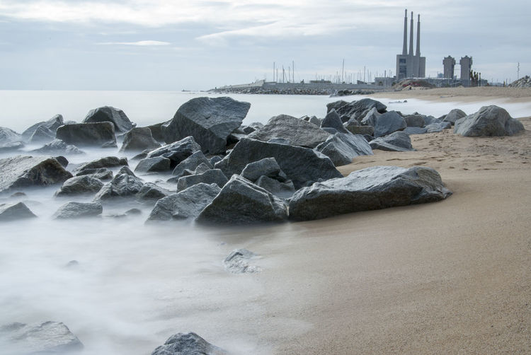 Rocks on shore at beach against harbor