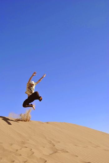 Man jumping in desert against clear blue sky