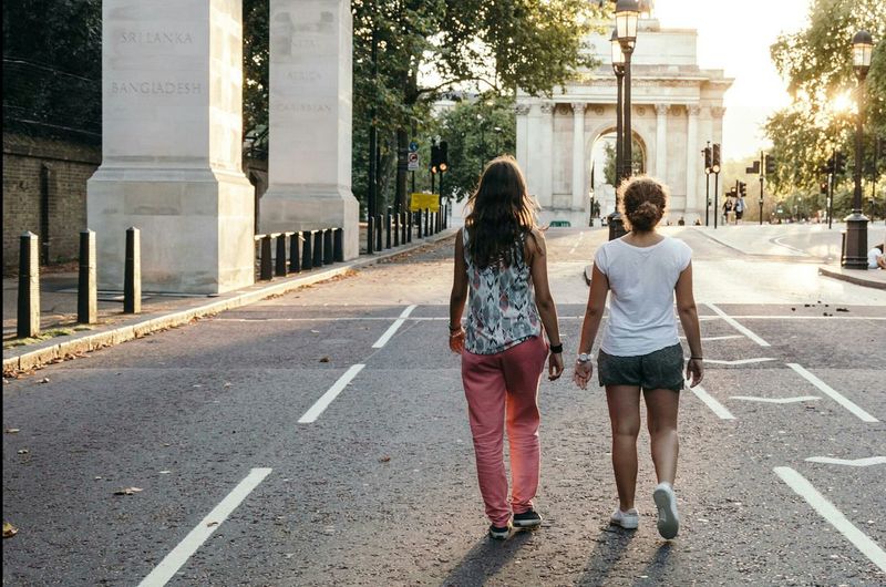 Full length rear view of friends walking on street by wellington arch at morning