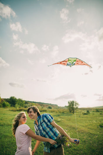 Couple flying kite on field against sky